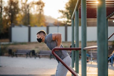 Genç bir adam gün batımında salgın sırasında spor sahasında maske takıp uyuşturucu kullanıyor. Spor, sağlıklı yaşam tarzı.