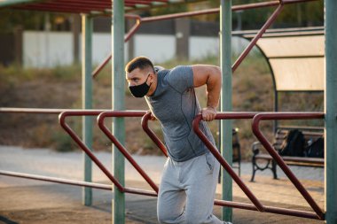 Genç bir adam gün batımında salgın sırasında spor sahasında maske takıp uyuşturucu kullanıyor. Spor, sağlıklı yaşam tarzı.