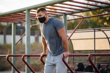 Genç bir adam gün batımında salgın sırasında spor sahasında maske takıp uyuşturucu kullanıyor. Spor, sağlıklı yaşam tarzı.