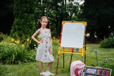 Okullu bir kız tahtaya ders yazıyor ve açık hava eğitimiyle meşgul. Okula dönüyorum, salgın sırasında öğreniyorum.