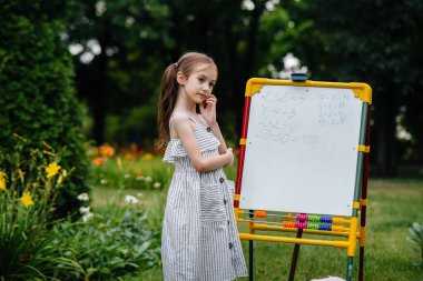Okullu bir kız tahtaya ders yazıyor ve açık hava eğitimiyle meşgul. Okula dönüyorum, salgın sırasında öğreniyorum.