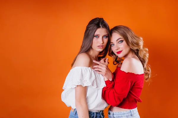 Dwie Młode Piękne Dziewczyny Pokazują Emocje Uśmiechy Studio Pomarańczowym Tle — Zdjęcie stockowe