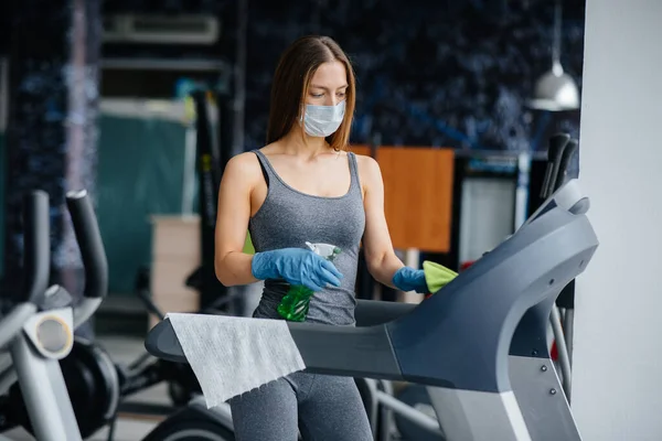 The girl in the mask disinfecting the gym equipment during a pandemic.