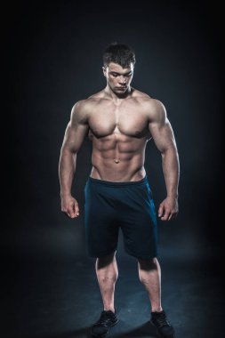 Stüdyoda siyah arka planda poz veren seksi genç bir atlet. Fitness, vücut geliştirme