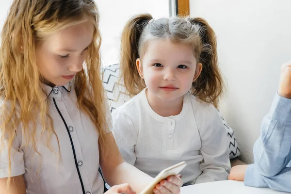 子供たちはカフェのテーブルに座り 携帯電話を一緒に再生します 近代芸能 — ストック写真