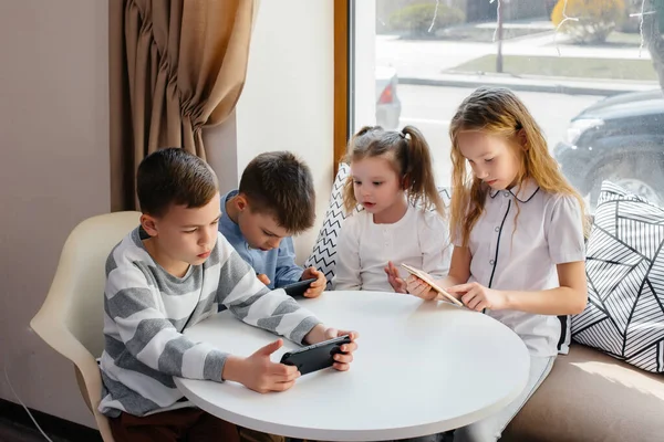 子供たちはカフェのテーブルに座り 携帯電話を一緒に再生します 近代芸能 — ストック写真