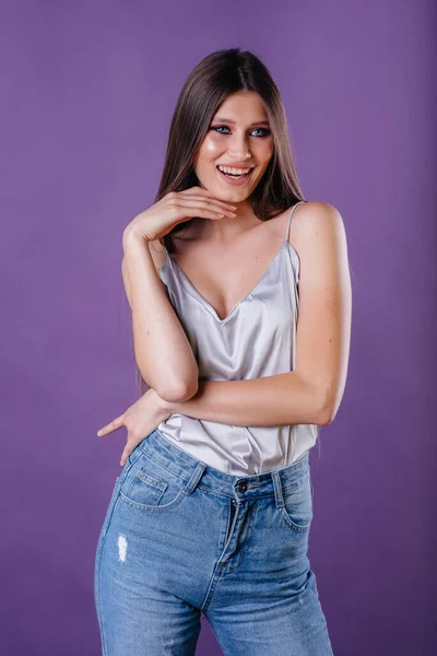 一个年轻漂亮的女孩在演播室里 在紫色的背景上表现出她的情感和微笑 女孩做广告 — 图库照片