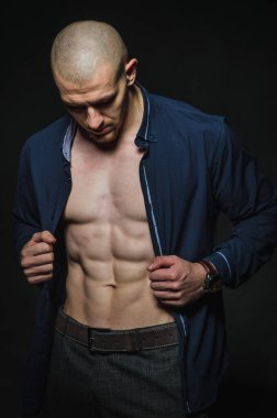 Tarz sahibi, kel genç bir adam çıplak bir gövdeyle kategoride karanlık bir arkaplanda duruyor.