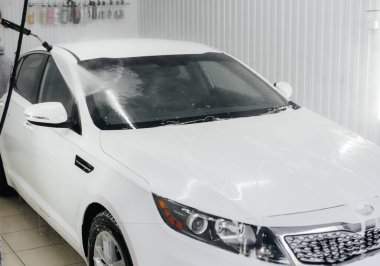 Köpüklü modern yıkama ve beyaz bir arabanın yüksek basınçlı suyu. Araba yıkama