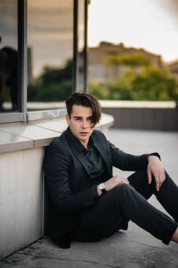 Şık bir genç adam gün batımında aynalı bir binanın yanında duruyor. Moda.