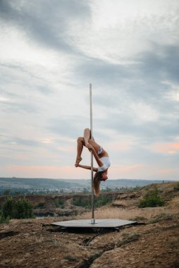 Genç ve seksi bir kız güzel bir günbatımında direğin üzerinde inanılmaz egzersizler yapıyor. Dans edelim. Cinsellik