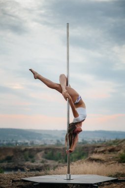 Genç ve seksi bir kız güzel bir günbatımında direğin üzerinde inanılmaz egzersizler yapıyor. Dans edelim. Cinsellik