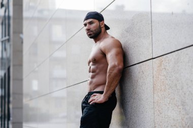 Seksi sporcu duvarın yanında üstsüz duruyor. Fitness, vücut geliştirme