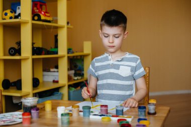 Odasında küçük sevimli bir çocuk oynuyor ve resim yapıyor. Eğlence ve eğlence. Evde kal.