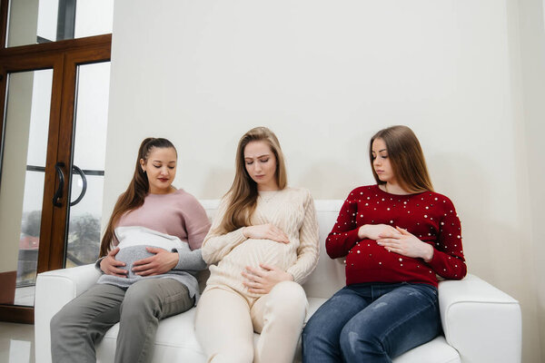 Pregnant girls sit on the couch and have fun chatting with each other. Pregnancy and taking care of the child's future
