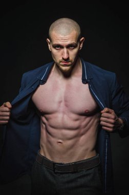 Tarz sahibi, kel genç bir adam çıplak bir gövdeyle kategoride karanlık bir arkaplanda duruyor.