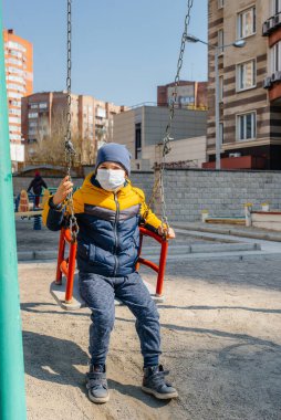 Karantina sırasında maskeli küçük bir çocuk oyun alanında yürüyor. Evde kal.