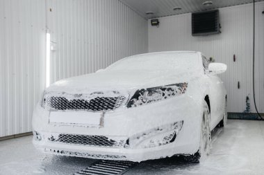 Köpüklü modern yıkama ve beyaz bir arabanın yüksek basınçlı suyu. Araba yıkama