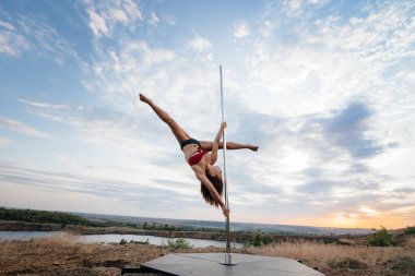 Genç ve seksi bir kız güzel bir günbatımında direğin üzerinde inanılmaz egzersizler yapıyor. Dans edelim. Cinsellik
