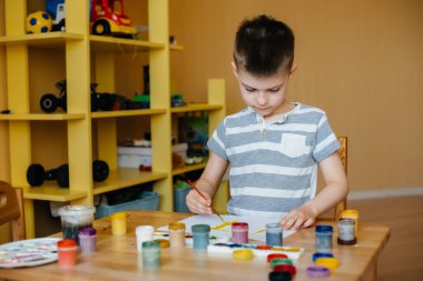 Odasında küçük sevimli bir çocuk oynuyor ve resim yapıyor. Eğlence ve eğlence. Evde kal.