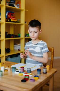 Odasında küçük sevimli bir çocuk oynuyor ve resim yapıyor. Eğlence ve eğlence. Evde kal.