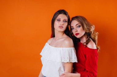 İki genç ve güzel kız, turuncu bir arka planda stüdyoda duygu ve gülümseme gösteriyor. Reklam için kızlar