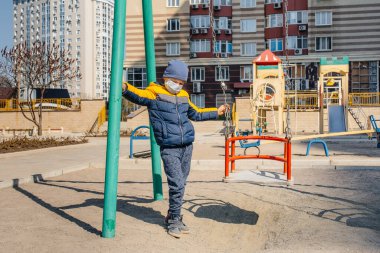 Karantina sırasında maskeli küçük bir çocuk oyun alanında yürüyor. Evde kal.