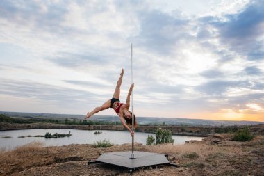 Genç ve seksi bir kız güzel bir günbatımında direğin üzerinde inanılmaz egzersizler yapıyor. Dans edelim. Cinsellik