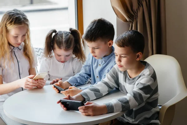 孩子们坐在咖啡馆的桌子旁 一起玩手机 现代娱乐 — 图库照片