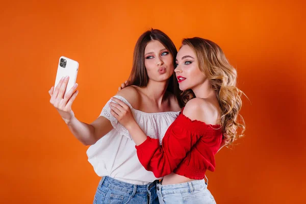 两个年轻漂亮的女孩带着一个自拍 在工作室里用紫色背景看手机 女孩做广告 — 图库照片