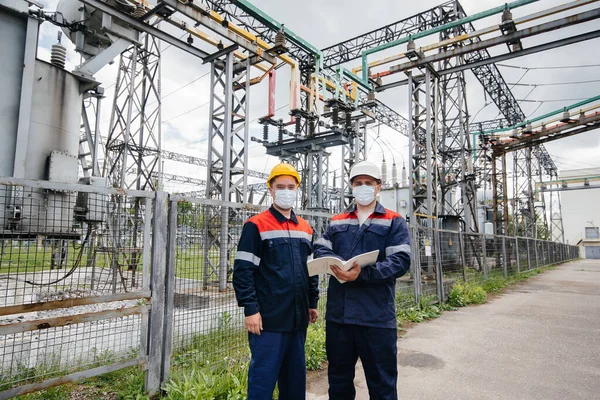 Engineers electrical substations conduct a survey of modern high-voltage equipment in the mask at the time of pandemia. Energy. Industry