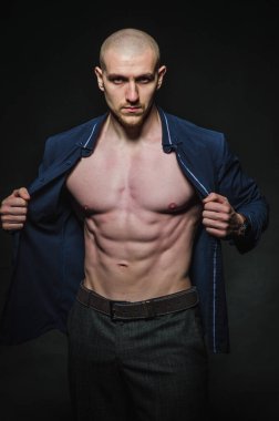 Tarz sahibi, kel genç bir adam çıplak bir gövdeyle kategoride karanlık bir arkaplanda duruyor.