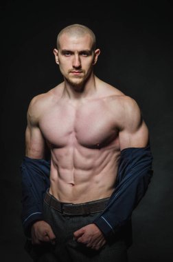 Tarz sahibi, kel genç bir adam çıplak bir gövdeyle kategoride karanlık bir arkaplanda duruyor.