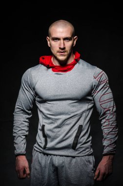 Stüdyoda kapüşonlu karanlık bir arka plana karşı duran sportif bir adam. Spor, güzellik