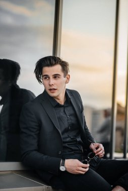 Şık bir genç adam gün batımında aynalı bir binanın yanında duruyor. Moda.