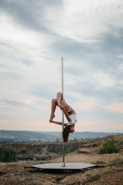 Genç ve seksi bir kız güzel bir günbatımında direğin üzerinde inanılmaz egzersizler yapıyor. Dans edelim. Cinsellik