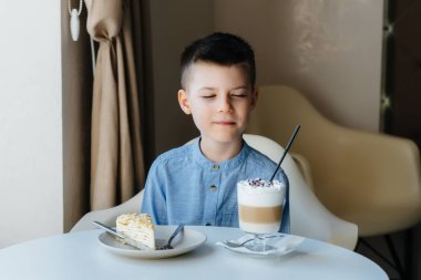 Küçük tatlı bir çocuk bir kafede oturuyor ve bir kek ve kakaoya yakından bakıyor. Diyet ve uygun beslenme