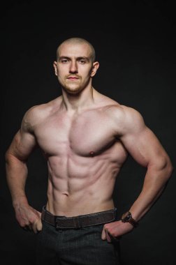 Sportif seksi adam karanlık bir zeminde üstsüz duruyor. Spor, güzellik