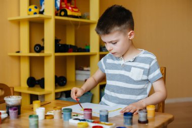 Odasında küçük sevimli bir çocuk oynuyor ve resim yapıyor. Eğlence ve eğlence. Evde kal.