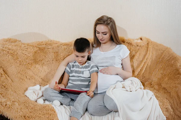 妊娠中のお母さんはタブレットのソファで息子と遊ぶ — ストック写真