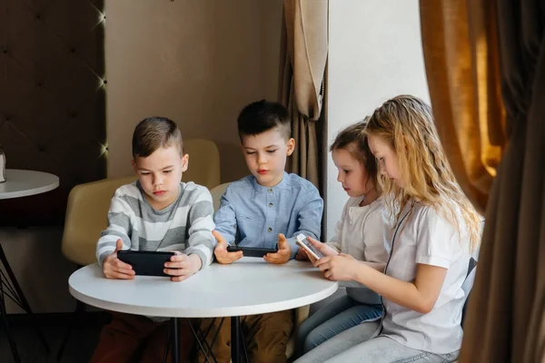 子供たちはカフェのテーブルに座り 携帯電話を一緒に再生します 近代芸能 — ストック写真