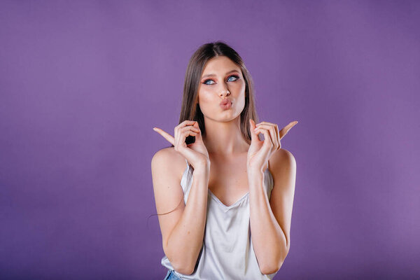 A young beautiful girl shows emotions and smiles in the Studio on a purple background. Girls for advertising