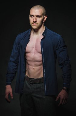 Tarz sahibi, kel genç bir adam çıplak bir gövdeyle kategoride karanlık bir arkaplanda duruyor.