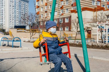 Karantina sırasında maskeli küçük bir çocuk oyun alanında yürüyor. Evde kal.