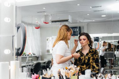 Güzel, modern bir güzellik salonunda, profesyonel bir makyöz genç bir kız için makyaj yapar. Güzellik ve moda.