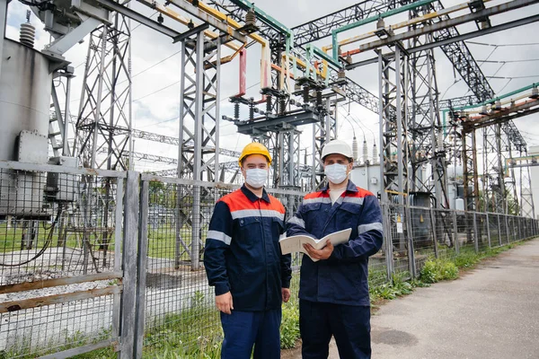 Engineers electrical substations conduct a survey of modern high-voltage equipment in the mask at the time of pandemia. Energy. Industry