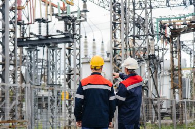 İki uzman elektrik santrali mühendisi modern yüksek voltajlı ekipmanları inceliyor. Enerji. Sanayi