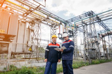 İki uzman elektrik santrali mühendisi akşamları modern yüksek voltajlı ekipmanları inceliyor. Enerji. Sanayi