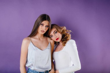 İki genç ve güzel kız, mor bir arka planda stüdyoda duygu ve gülümseme gösteriyor. Reklam için kızlar