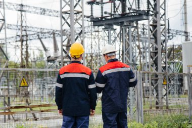 İki uzman elektrik santrali mühendisi modern yüksek voltajlı ekipmanları inceliyor. Enerji. Sanayi